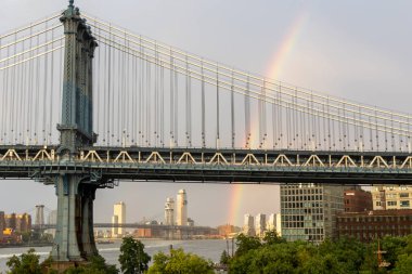 Kısa bir yağmurun ardından New York 'taki Manhattan Köprüsü' nün üzerinde bir gökkuşağı güzellikle uzanır, yakınlardaki binalarla ve aşağıdaki nehirle çelişir..