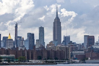 New York şehrinin ufuk çizgisi tarihi ve modern gökdelenlerin bir karışımını sergiliyor, ikonik Empire State Binası belirgin bir şekilde mavi gökyüzüne karşı yükseliyor..