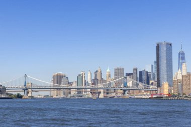 Manzara ikonik Brooklyn Köprüsü 'nü yakalıyor Doğu Nehri' ni kaplıyor, Manhattan silueti yüksek binalar ve berrak mavi gökyüzü ile, kentsel güzelliği vurguluyor..