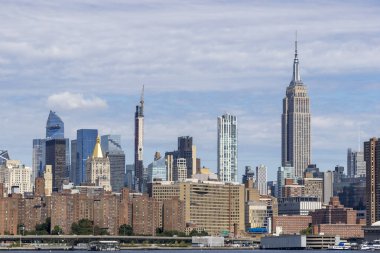 New York şehrinin ufuk çizgisi tarihi ve modern gökdelenlerin bir karışımını sergiliyor, ikonik Empire State Binası belirgin bir şekilde mavi gökyüzüne karşı yükseliyor..