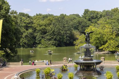 Visitors gather around the iconic Bethesda Fountain in Central Park, taking in the warm sunshine and vibrant greenery while enjoying various activities. clipart