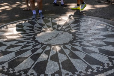 İnsanlar Central Park 'ta sıcak bir günün tadını çıkarıyorlar. John Lennon' a adanmış sembolik bir mozaiğin yanında duruyorlar. Huzurlu bir atmosfer ve ağaçlarla çevrili..