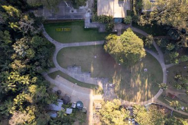 Sao Paulo 'daki yüksek gökdelenlerin arasına kurulmuş geniş bir şehir parkı, güneşli bir öğleden sonra açık havada eğlenen insanlarla dolu yemyeşil ve patikalarla dolu..