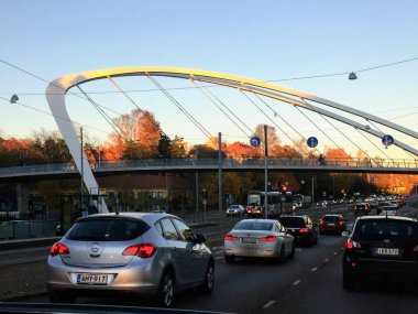 Şehir manzarası, caddenin aşağısındaki şık modern tasarım yaya geçidine birkaç araba, yön işaretleri, kablolara asılı lambalar ve arka plandaki tramvayla birlikte sonbahar güneşi altında.