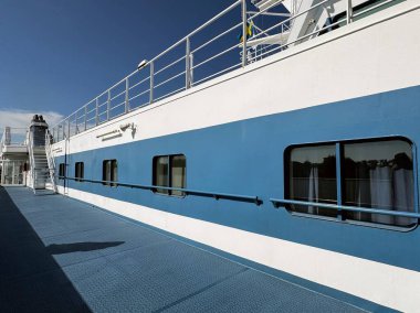 Beyaz-mavi gemi duvarlı boş feribot güvertesi, güneşli hava ve deniz yolculuğunda uzun gölgeler.
