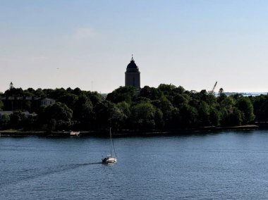 Güneşli bir yaz gününde Suomenlinna Kilisesi 'nin arka planında Suomenlinna adasından geçen küçük bir yelkenli.