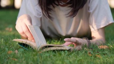Genç ve çekici bir kız yeşil çimlerde uzanıyor ve kitap okuyor.