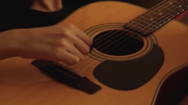 Evde akustik gitar çalan genç bir kadın.