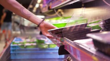 Bir kadın buzdolabından paketlenmiş et alıyor. Süpermarket