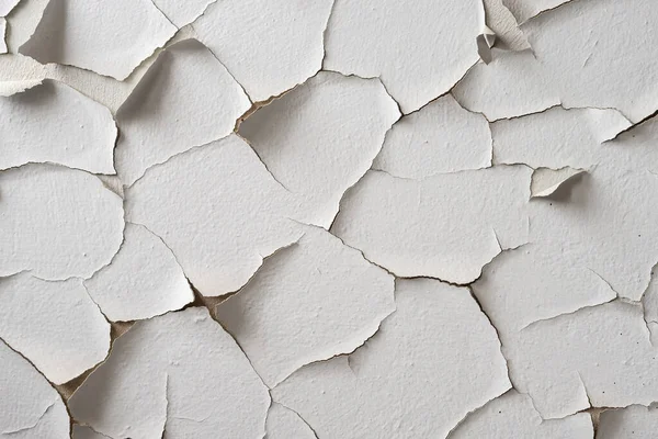 White painted wall with cracks and pieces of peeling paint. Flaky paint