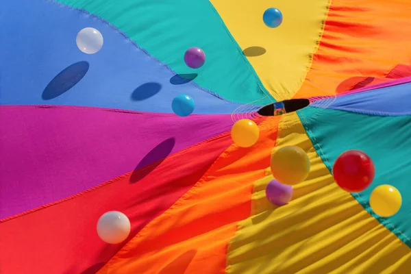 Multicolor-patterned kids play parachute with colorful bouncing balls. Rainbow colors toys for outdoor activities