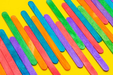 Yanyana dizilmiş renkli buzlu çubuklar. Sarı kağıt üzerinde tahta dondurma çubukları. Çok renkli arkaplan
