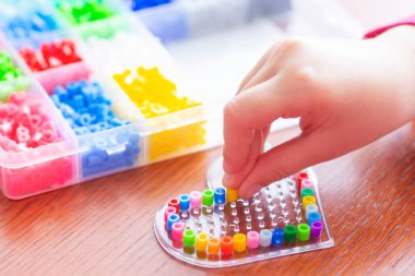 Çocuk kalp şeklinde plastik bir şablona renkli boncuklar koyuyor. Bir çocuğun eli yakındı. Eğitim kavramı