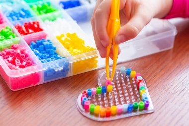 Renkli boncuk kalp yapmak için plastik cımbız kullanan bir kız eli.