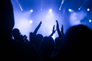 Sahnenin önündeki bir konserde mavi tonlu parlak spot ışıklarıyla bir kalabalığın silueti. Müzik canlı performans