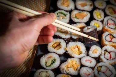 Adam servis tepsisinden suşi rulosunu alıyor.