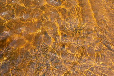 Yüzeyinde dalgalanmalar ve güneş parıltısı olan sığ nehir suyu. Soyut arkaplan dokusu