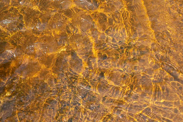 Yüzeyinde dalgalanmalar ve güneş parıltısı olan sığ nehir suyu. Soyut arkaplan dokusu