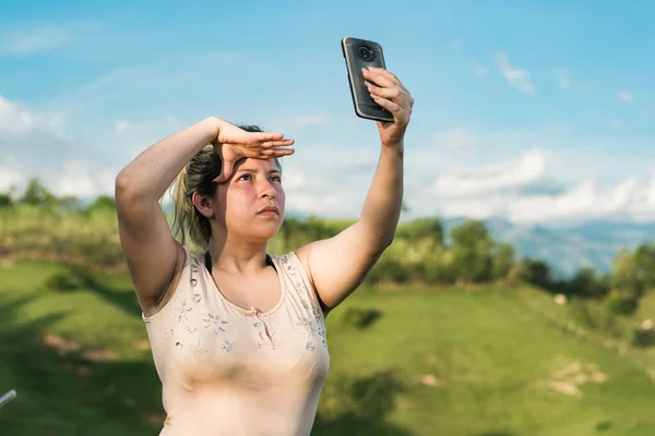 beautiful young latina woman on top of a colombian mountain looking for a signal for her mobile phone. girl looking for satellite reception on top of a hill.