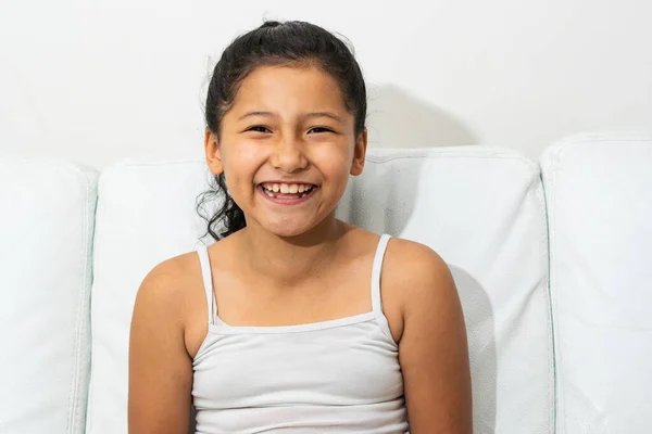 ラテン系のブルネットの女の子の肖像 ソファに座って笑顔と彼女の歯を見せて インドの特徴を持つ女の子 ストックフォト
