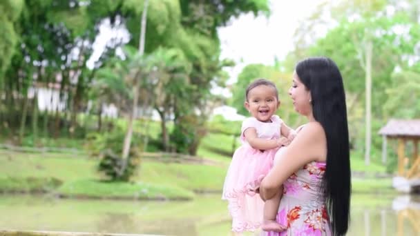 年轻的拉蒂娜妈妈把她的女婴抱在湖边 美丽的黑发宝宝在妈妈身边笑得很开心 — 图库视频影像