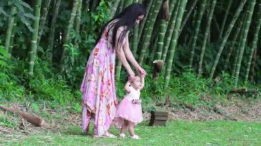 Genç Latin anne bebeğine çimenlerde yürümeyi öğretiyor, bambu ormanının ortasında yürüyor..