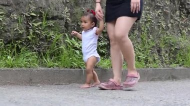 Küçük bebeğine yürümeyi öğreten genç bir anne. Latin bir kadın sokakta yürürken bebeğini elinden tutuyor..