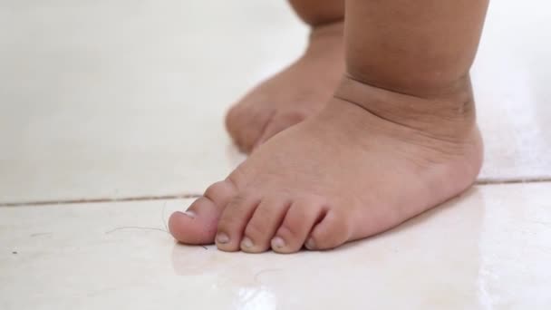 歩く方法を学ぶために白い床の上に立つ茶色の赤ん坊の足の詳細なビュー — ストック動画