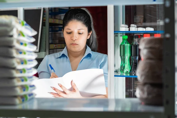 young woman, working in a store, organizing and writing down a list of existing products.