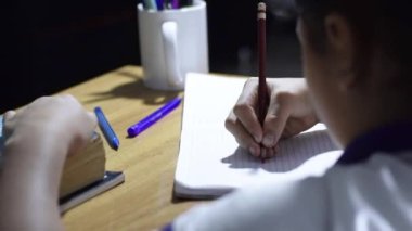 Küçük Latin bir kızın, esmer, ahşap bir masanın üzerine deftere resim çizen bir fotoğrafı. Karanlık bir yerde ders çalışmak..