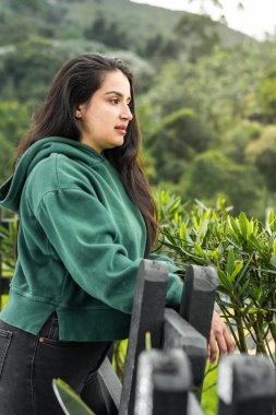 beautiful latina girl standing next to a wooden fence enjoying the fresh air