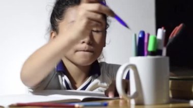 close-up of a little Latina girl, doing her homework, while taking pens out of a white cup.