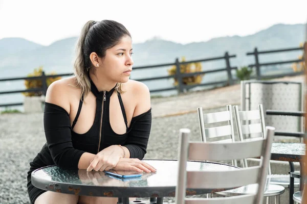 young latina woman, sitting waiting for the food she ordered, in an open-air restaurant