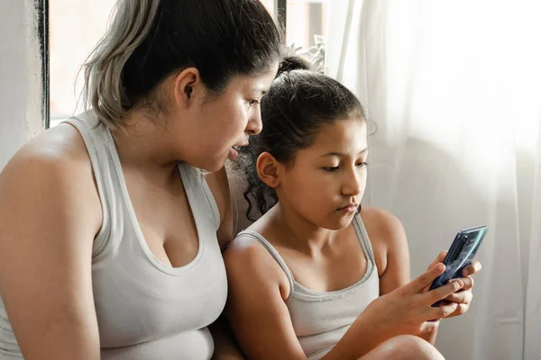 mother and daughter, together looking at the content of social networks on the cell phone