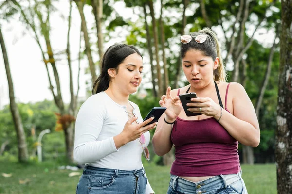 Deux Latines Regardant Leurs Téléphones Portables Dans Parc Faisant Une — Photo