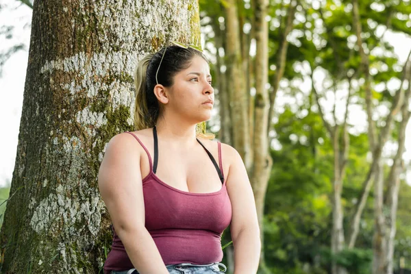 Νεαρή Λατίνα Γυναίκα Κάθεται Δίπλα Ένα Δέντρο Ένα Πάρκο Ψάχνει — Φωτογραφία Αρχείου