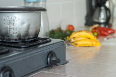 Sobanın üstündeki gri tencereye yakın çekim, yemek pişirme. arka planda meyve ve sebzeler.