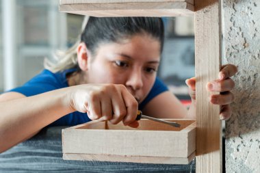 Genç Latin bir kadın, ahşap bir rafı tornavidayla birleştiriyor, işine çok odaklanmış..