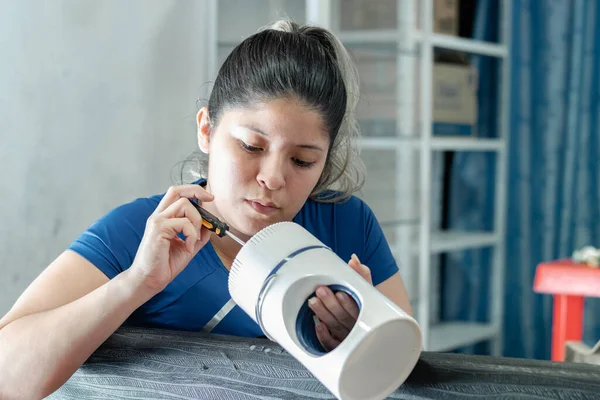 stock image close-up of a young latina woman trying to disassemble a fan with a screwdriver