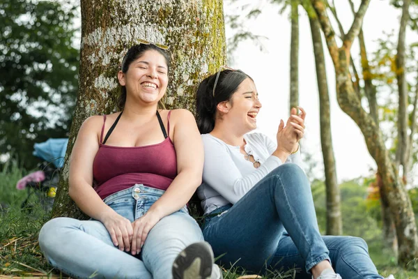 两个非常快乐的拉丁女孩在公园的一棵树旁嬉笑着 — 图库照片