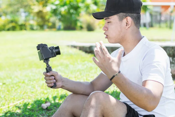 Young Latino man creating a video vlog, explaining the progress of his summer trip, holding the camera with his hand.