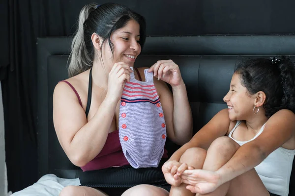 Joven Madre Latina Con Pequeña Hija Morena Mostrando Ropa Bebé — Foto de Stock