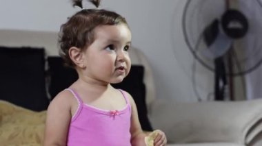 Kafkasyalı güzel Latin bebek oturma odasında patates kızartması yerken başını yana doğru sallıyor.