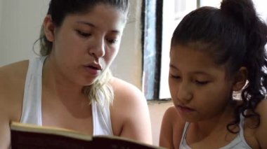 Genç Latin annenin genç kızına kitap okuduğu yakın plan çekimler. Kızı onu izleyip dinlerken çok konsantre olmuş..