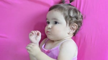 Küçük Latin bir kızın yemeğini çiğneyen, pembe bir şiltenin üzerinde yattığı yakın plan.