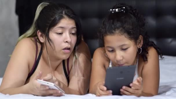 Madre Hija Latinas Tumbadas Cama Mirando Teléfono Celular Tableta Mientras — Vídeos de Stock