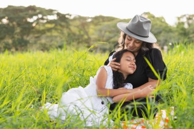 Annesi onu okşarken, küçük kızı gözleri kapalı şekilde göğsüne uzanmış bir şekilde yerde oturan genç Latin bir anne.