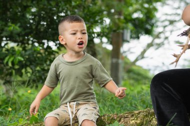 Beyaz Latin köylü çocuk bağırıyor, yerdeki bir ağacın gövdesinde oturuyor.