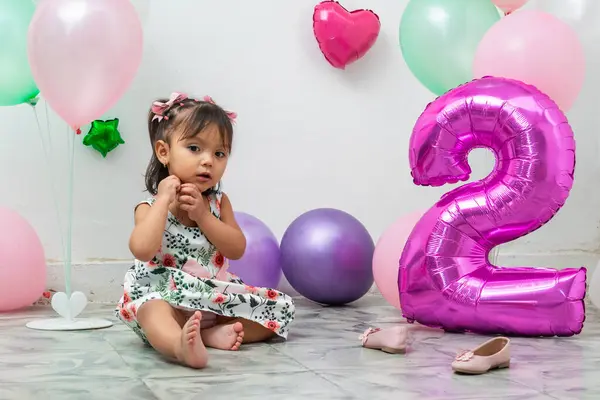 stock image small latin brunette girl sitting on the floor without shoes next to a large balloon shaped like the number two