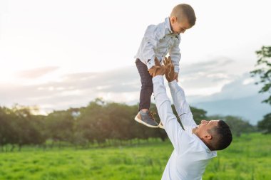 Genç Latin baba oğlunu yukarı çekiyor, arka planda günbatımıyla oynuyor.